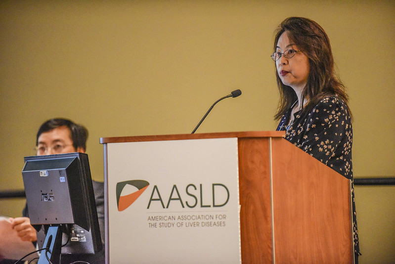 A woman of Asian descent stands at a podium to present research during The Liver Meeting.